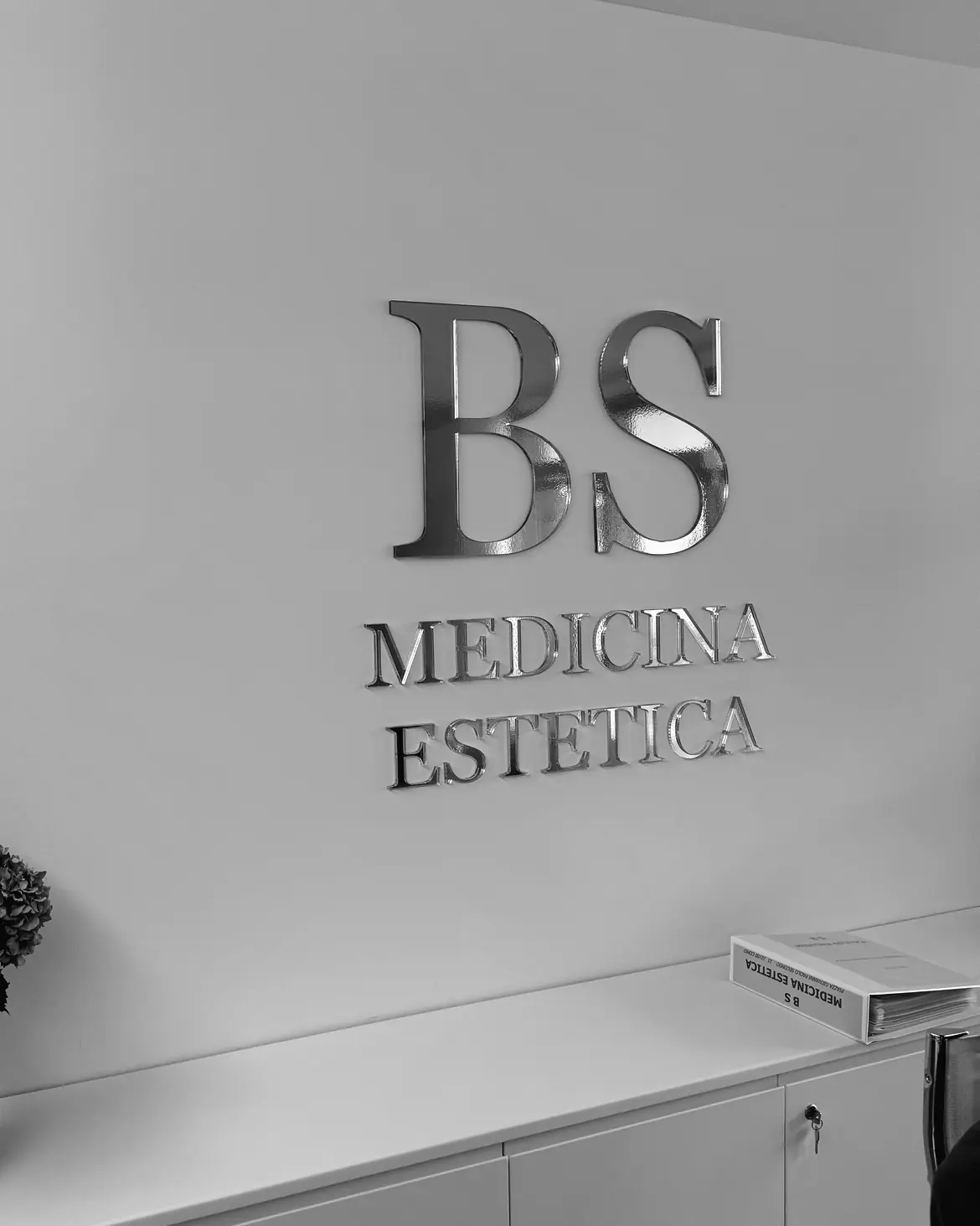 L'ingresso dello studio di Como: il monogramma BS in metallo sulla parete bianca.
